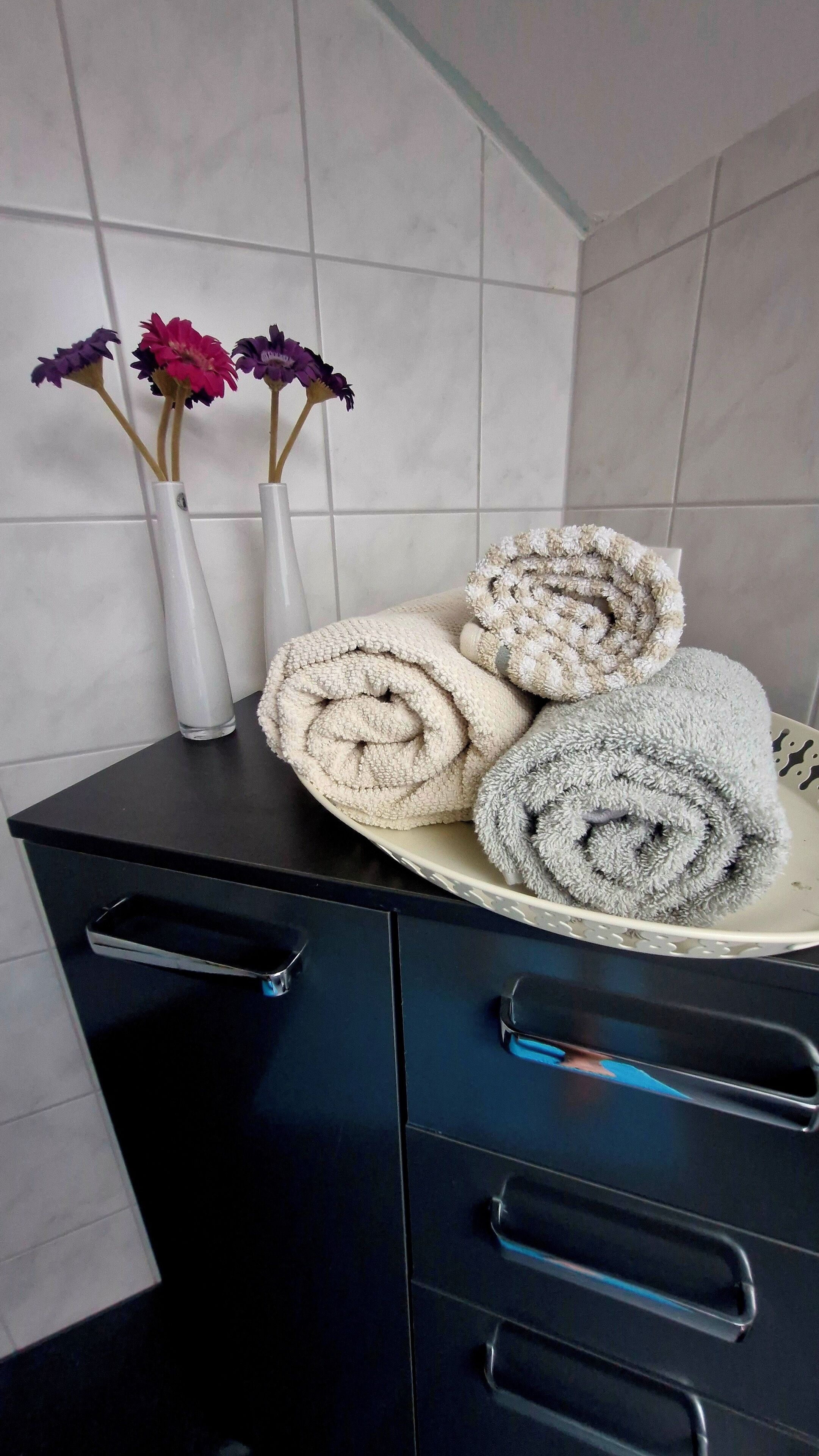 A bathroom with a black cabinet, a white sink, and a towel rack with rolled towels.