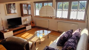 Una sala de estar con televisor, guitarra, una mesa de centro de vidrio y un sofá con cojines estampados.