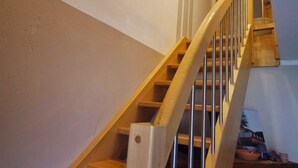 Un escalier en bois avec une rampe, un tableau encadré accroché au mur et un meuble en bois au bas de l’escalier.