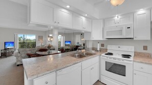 A modern kitchen with white cabinets, a built-in microwave, and a large island with a sink. - Vacation At Admiral's Bay 148! Fun In The Sun! 2B/2B Condo Walk To Beach! (Fort Myers Beach)