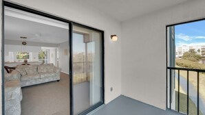 A modern apartment with a sliding glass door leading to a balcony, a sofa, and a kitchen area visible through the door. - Vacation At Admiral's Bay 148! Fun In The Sun! 2B/2B Condo Walk To Beach! (Fort Myers Beach)
