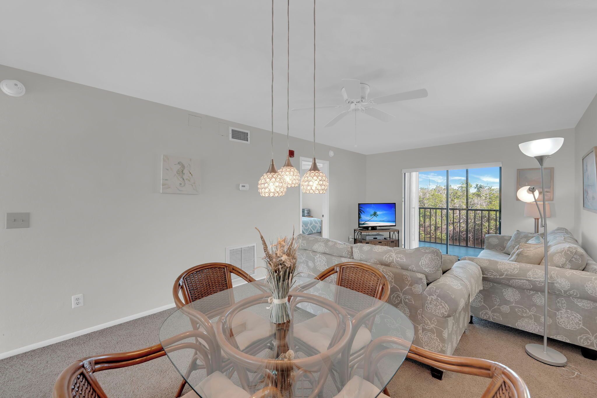 A modern living room with a glass dining table, wicker chairs, a sofa set, and a ceiling fan.