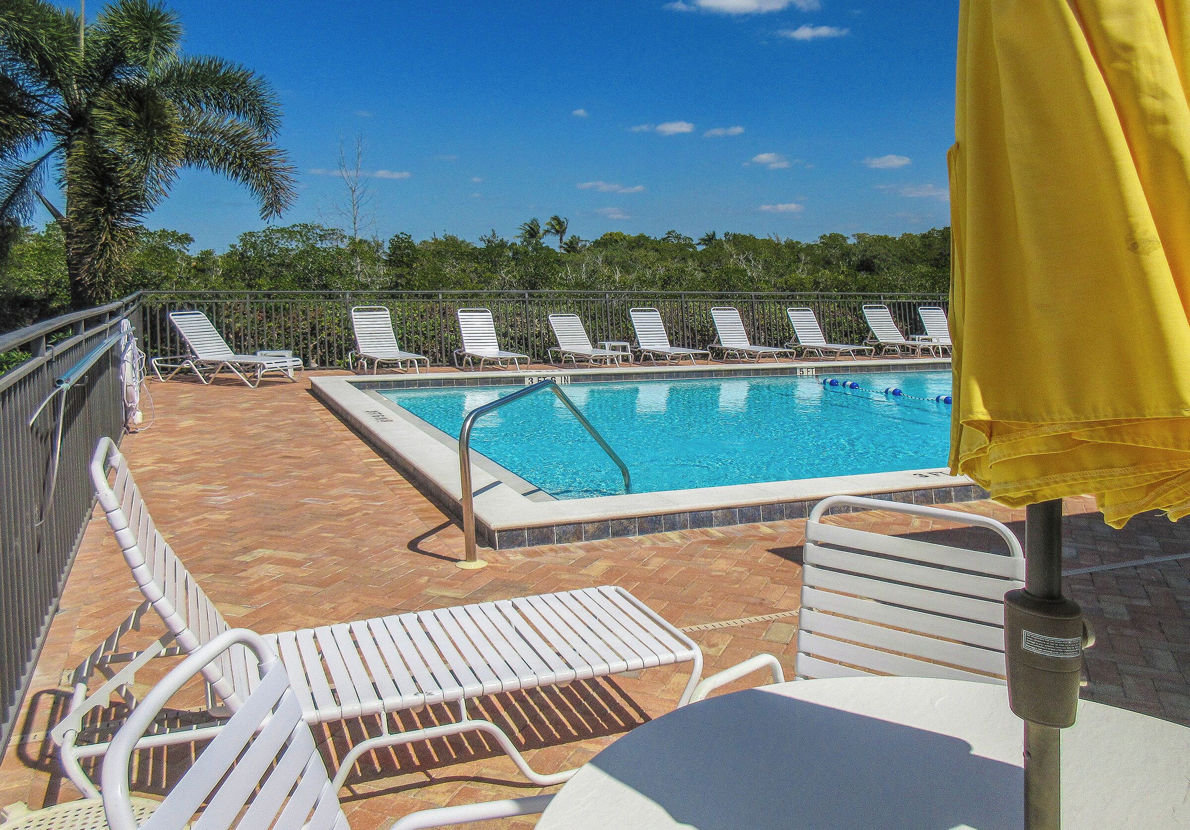 Zona de piscina con sillas de descanso y un paraguas amarillo.