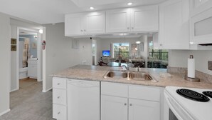 A modern kitchen with white cabinets, a granite countertop, a built-in oven, and a stainless steel sink. - Vacation At Admiral's Bay 148! Fun In The Sun! 2B/2B Condo Walk To Beach! (Fort Myers Beach)