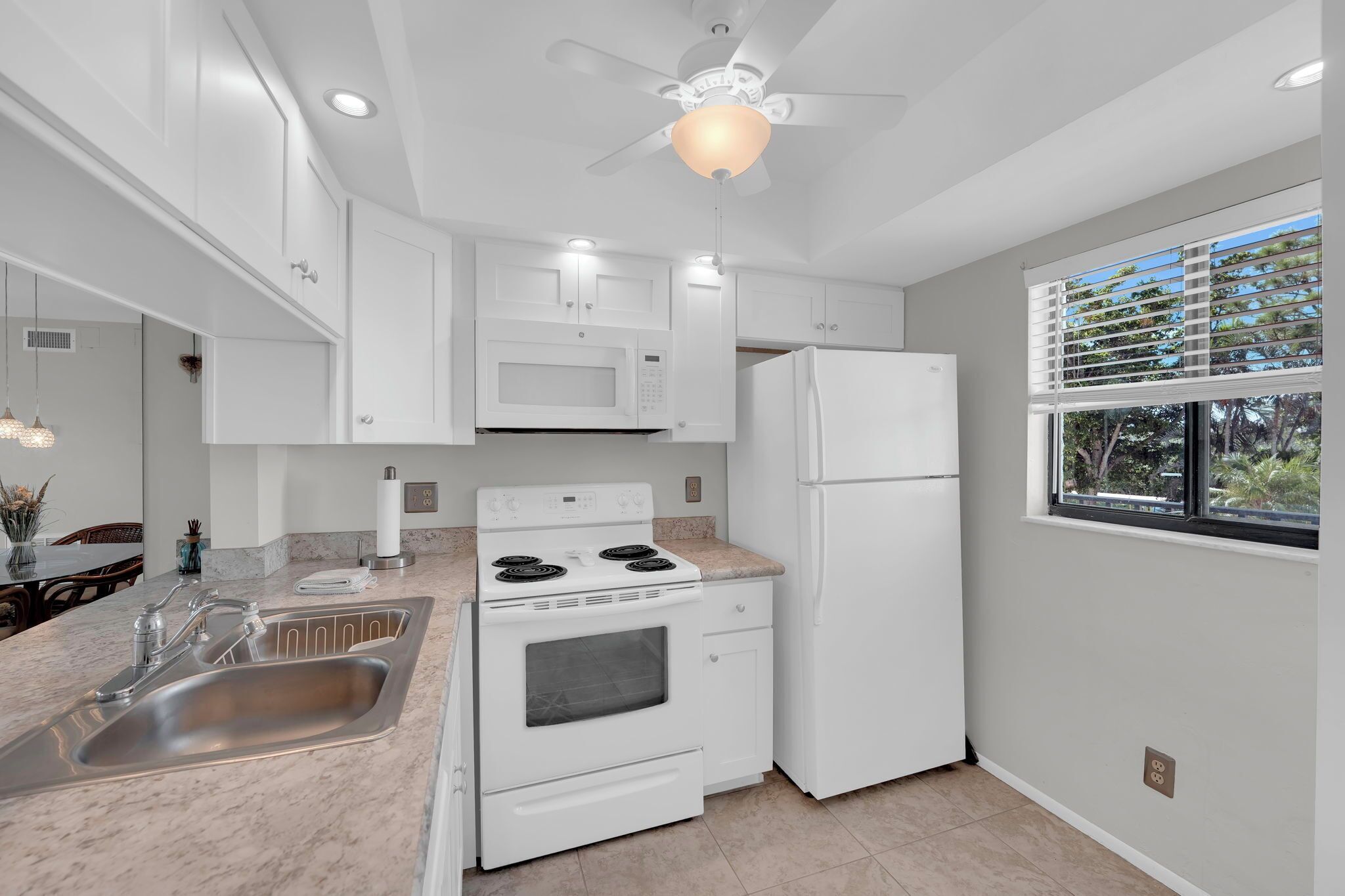 A modern kitchen with white appliances, a granite countertop, and a window with blinds.