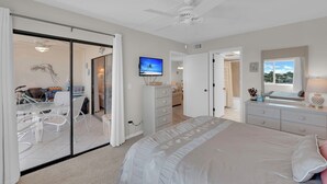 Une chambre à coucher comprenant un lit, une télévision, une commode et une porte-fenêtre coulissante donnant sur un balcon.