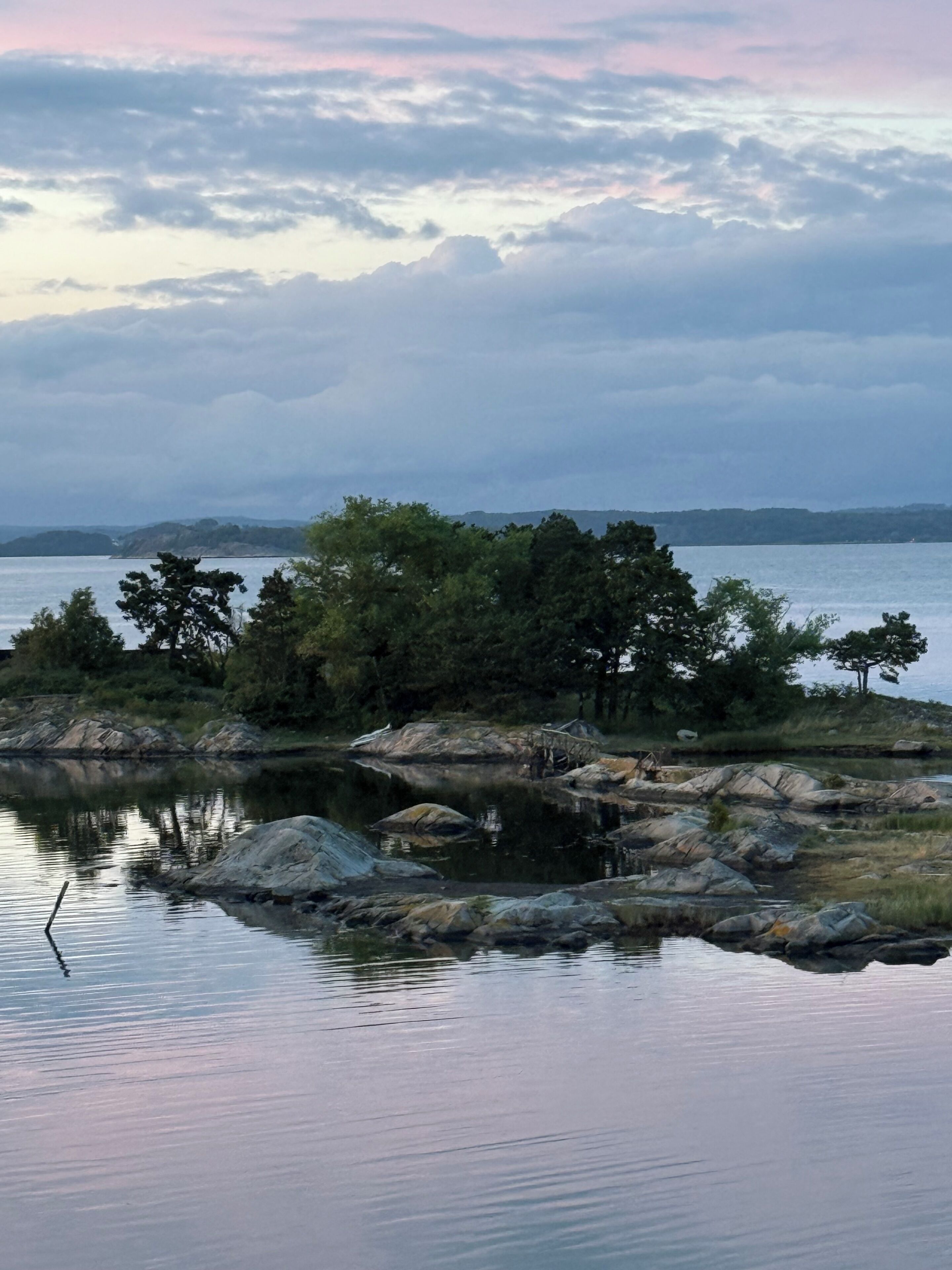 A tranquil lakeside scene with a small island featuring a wooden bridge and rocky terrain.