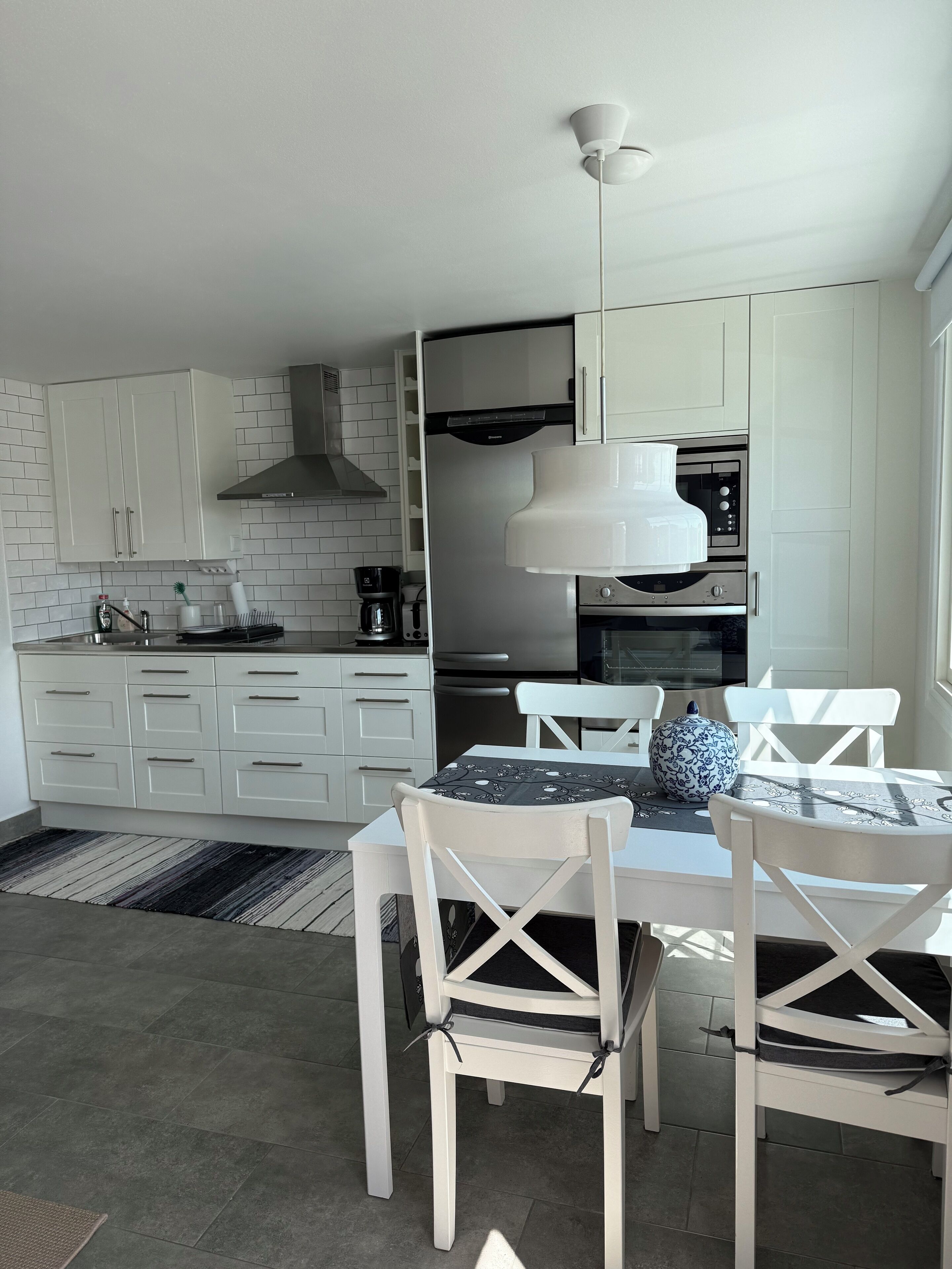 A modern kitchen with white cabinets, a built-in oven, and a dining area with white chairs and a table.