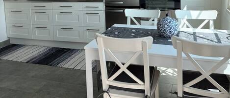 A modern kitchen with white cabinets, a built-in oven, and a dining area with white chairs and a table.