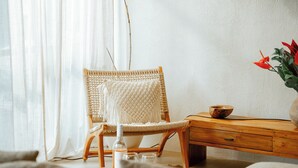 A wicker chair with a macrame cushion, a wooden side table with a bowl, and a vase with red flowers. - Heart Villa Berawa (Canggu)