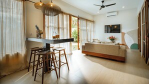 A modern living room with a sofa, a dining area with stools, and a kitchen counter. - Heart Villa Berawa (Canggu)