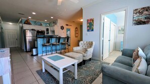 Un espacio habitable compacto con kitchenette, una zona de comedor con taburetes de bar, un sillón estampado, un sofá y una alfombra.