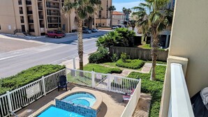 Un balcón con piscina, vista a una calle con coches y un edificio de varios pisos al fondo.