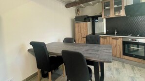 A modern kitchen with a dining area, featuring exposed wooden beams, a large dining table with chairs, and a built-in oven. - Maison cosie with fenced garden " DucnVosges " (Champ-le-Duc)