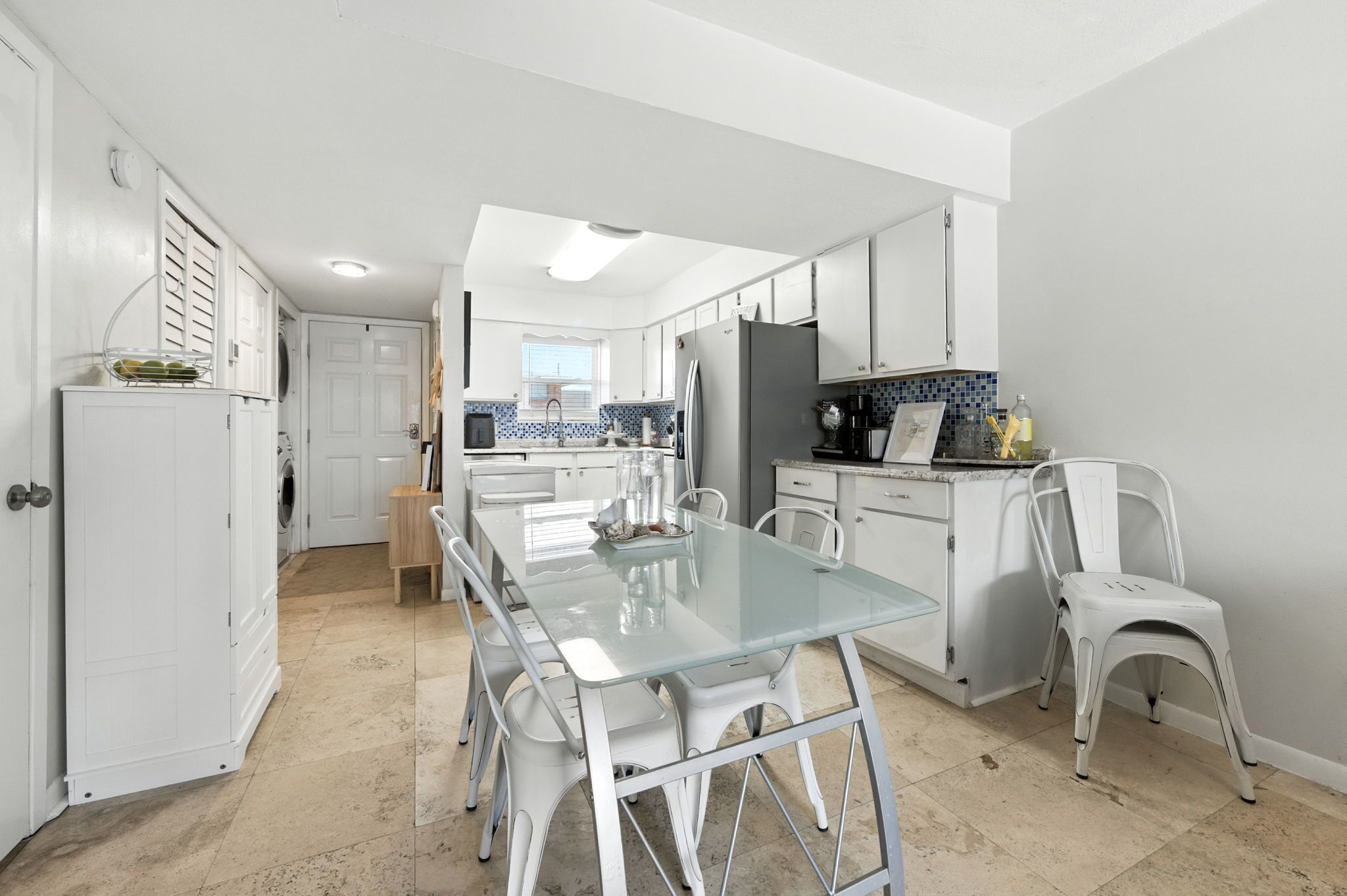 Una cocina moderna con armarios blancos, una mesa de comedor de vidrio y sillas blancas.
