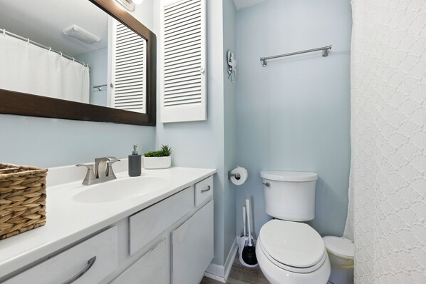 Un baño con lavamanos blanco, un espejo, toallero, inodoro y cortina de ducha.