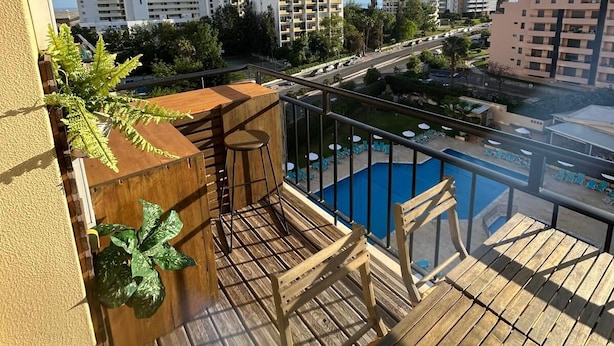 Un balcon doté d’une terrasse en bois, d’une piscine et offrant une vue sur les bâtiments environnants.
