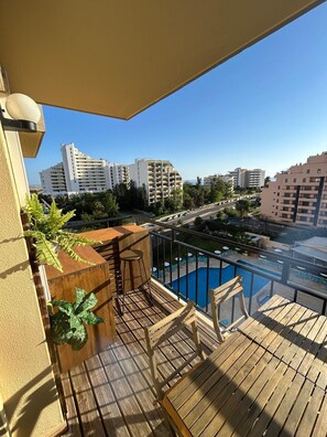 A balcony with a wooden deck, a pool, and a view of surrounding buildings. - Mar de Amarilis - comfy 1 bedroom Apartment sea view close to Rocha Beach (Portimão)