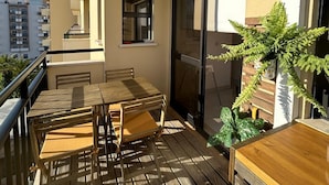 Un balcon avec une table et des chaises en bois, une plante en pot et une porte-fenêtre coulissante.