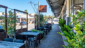 An outdoor café with tables and chairs, a street view, and a building with a sign.
