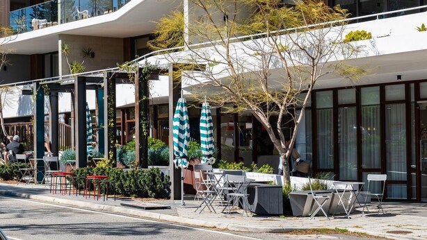 A modern building with outdoor seating and a tree in front.