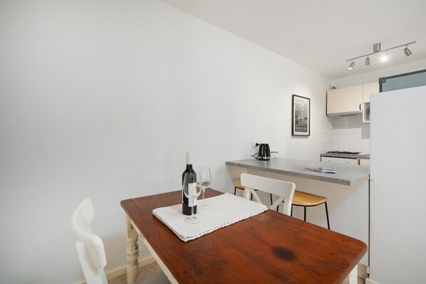 Una cocina compacta con una mesa de madera, una silla blanca y una pequeña isla con un hervidor.