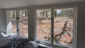 A bedroom with a large window, a bed, and a view of a wooded area. - Quiet Pine Retreat in Tawas City (Tawas City)