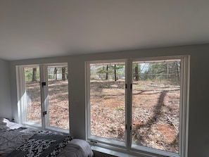 A bedroom with a large window, a bed, and a view of a wooded area.