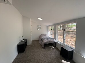 A bedroom with a bed, a dresser, a mirror, and a window with a view of trees.