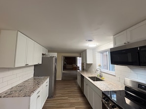 A modern kitchen with white cabinets, granite countertops, a stainless steel refrigerator, a built-in microwave, and a dishwasher.