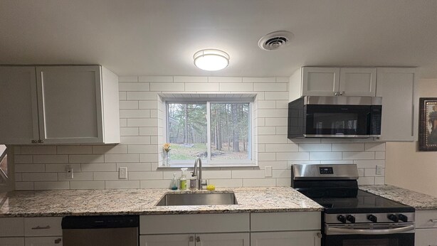 A kitchen with white cabinets, a stainless steel stove, a microwave, and a window with a view of trees. - Quiet Pine Retreat in Tawas City (Tawas City)