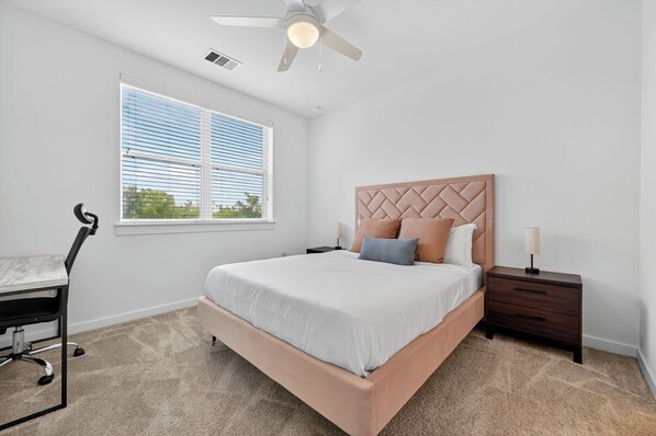 A bedroom with a bed, a desk, a chair, a nightstand, a lamp, and a ceiling fan.