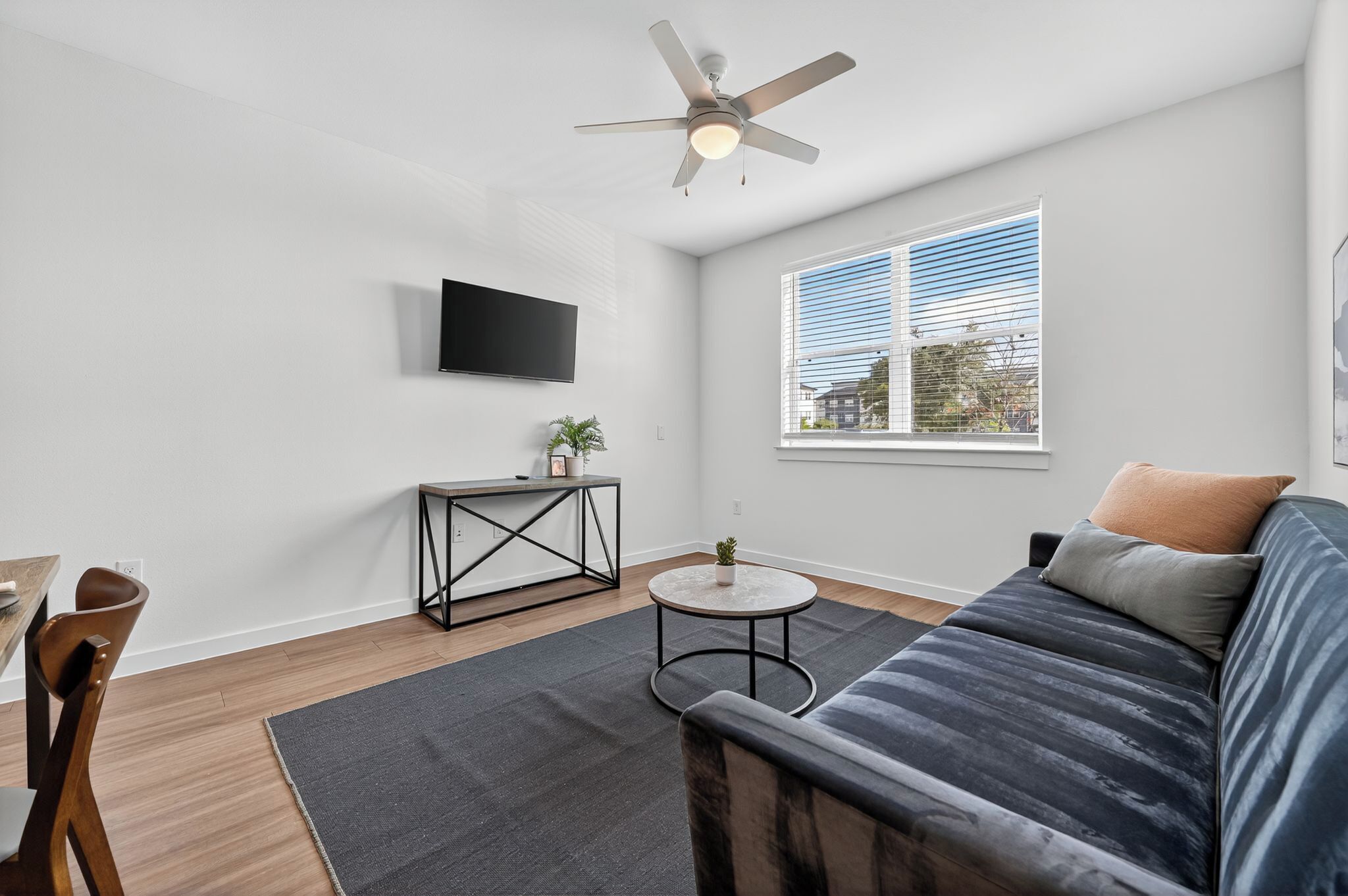 Un salon moderne avec un canapé, une table basse, un téléviseur fixé au mur et un ventilateur de plafond.