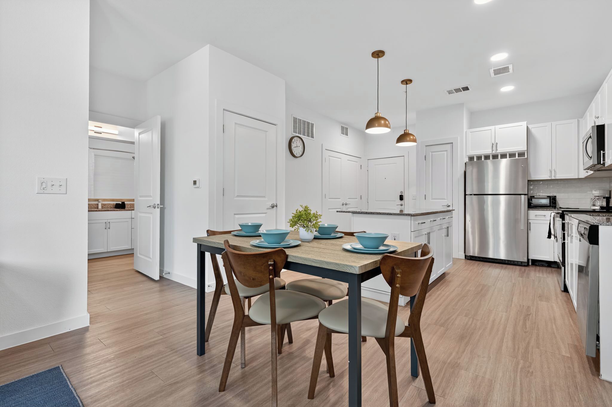 A modern kitchen with white cabinets, stainless steel appliances, and a wooden dining table with blue bowls.