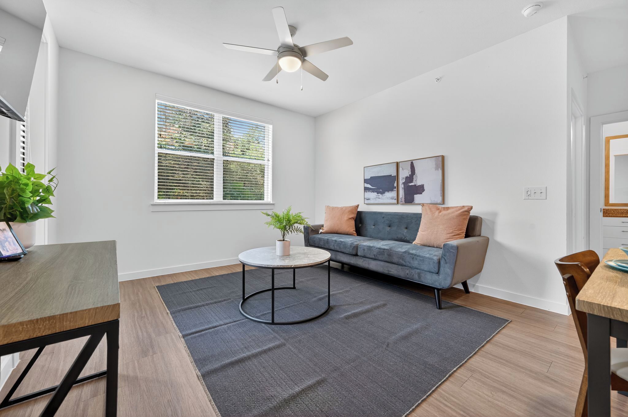 Een moderne woonkamer met een grijze bank, een ronde salontafel en een plafondventilator.