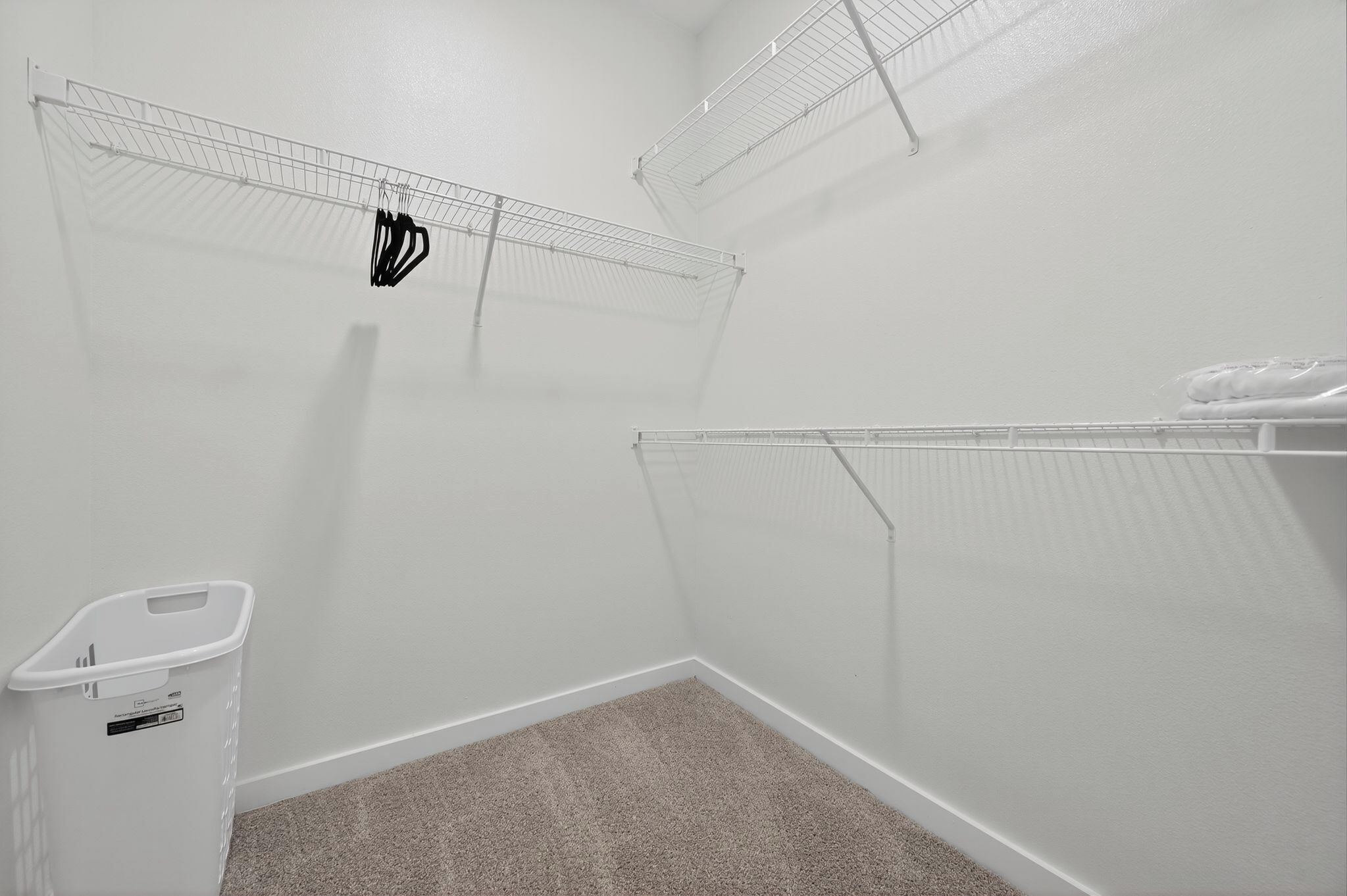 A clean, white room with a carpeted floor, a white trash bin, and wire shelving units.