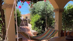 Un patio con una hamaca, un sillón de macramé y una mesa redonda de madera con una cesta tejida.