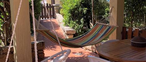 A patio area with a hammock, macrame chair, and a round wooden table with a woven basket.