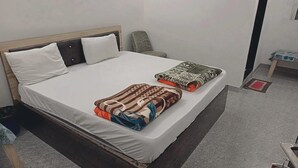 A bed with a patterned blanket and pillows, a bedside table with a lamp, and a wall-mounted shelf. - Hotel Shree Shyam Khatushyamji (Danta Ramgarh)