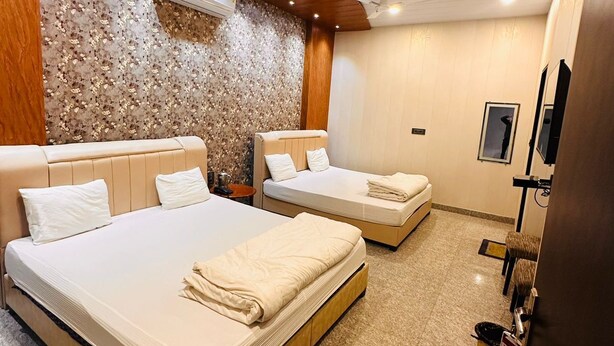 A hotel room with two beds, a ceiling fan, a stone wall, and a television. - Hotel Shree Shyam Khatushyamji (Danta Ramgarh)