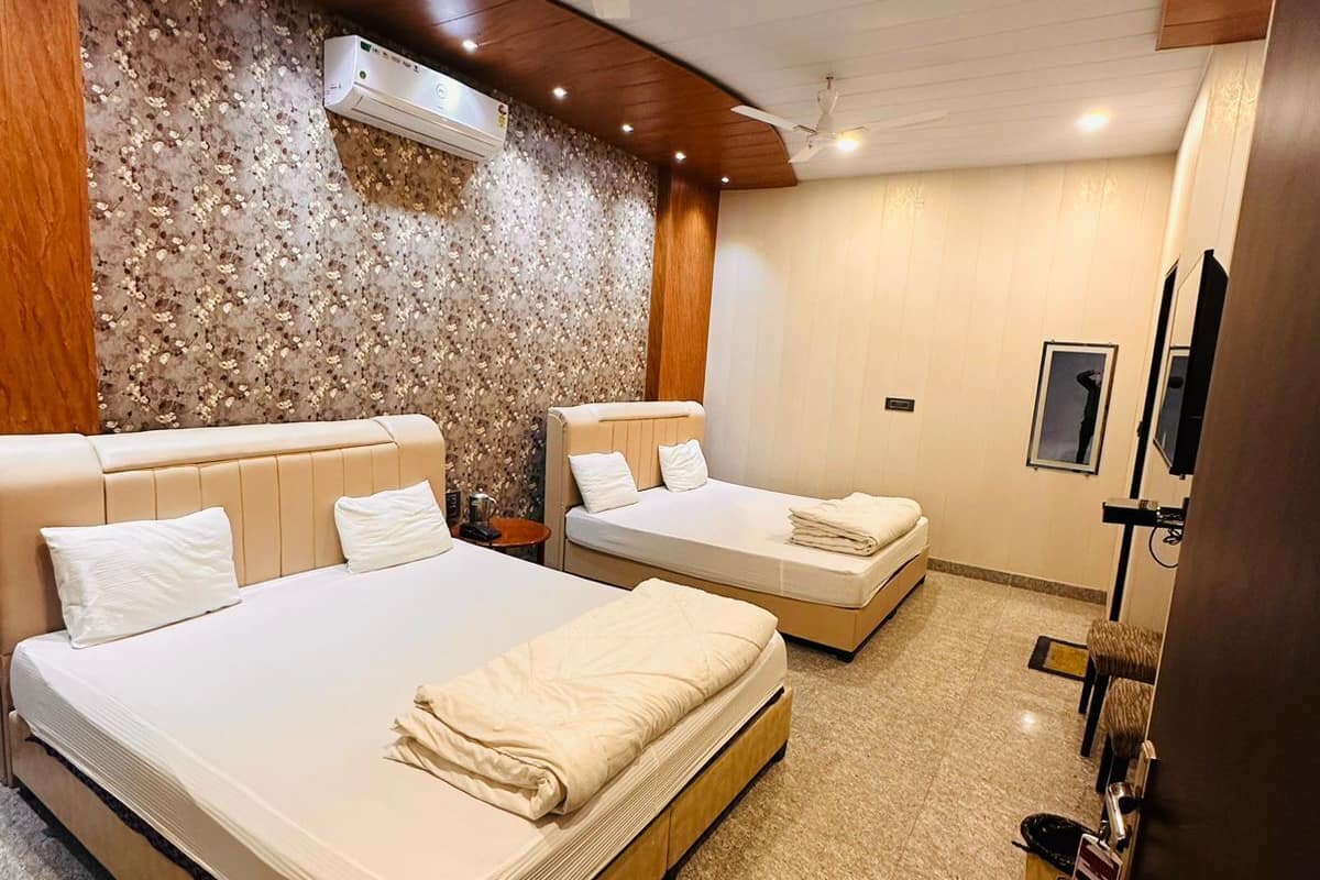 A hotel room with two beds, a ceiling fan, a stone wall, and a television.