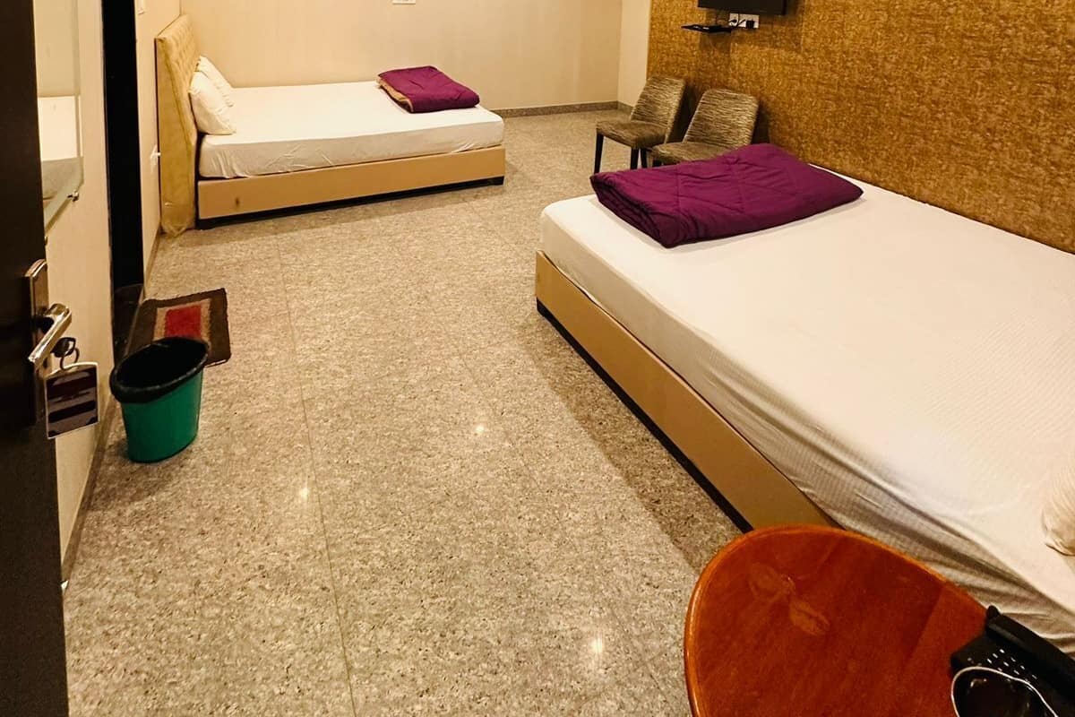 A hotel room with two beds, a ceiling fan, an air conditioning unit, a television, and a small trash bin.