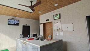 A reception area with a marble counter, a ceiling fan, a television, and a sign indicating the location. - Hotel Shree Shyam Khatushyamji (Danta Ramgarh)