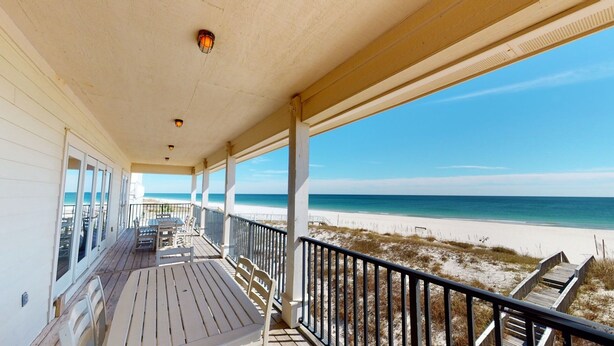 Un espace extérieur abrité, avec vue sur la plage, comprenant une terrasse en bois, des chaises et une rambarde.
