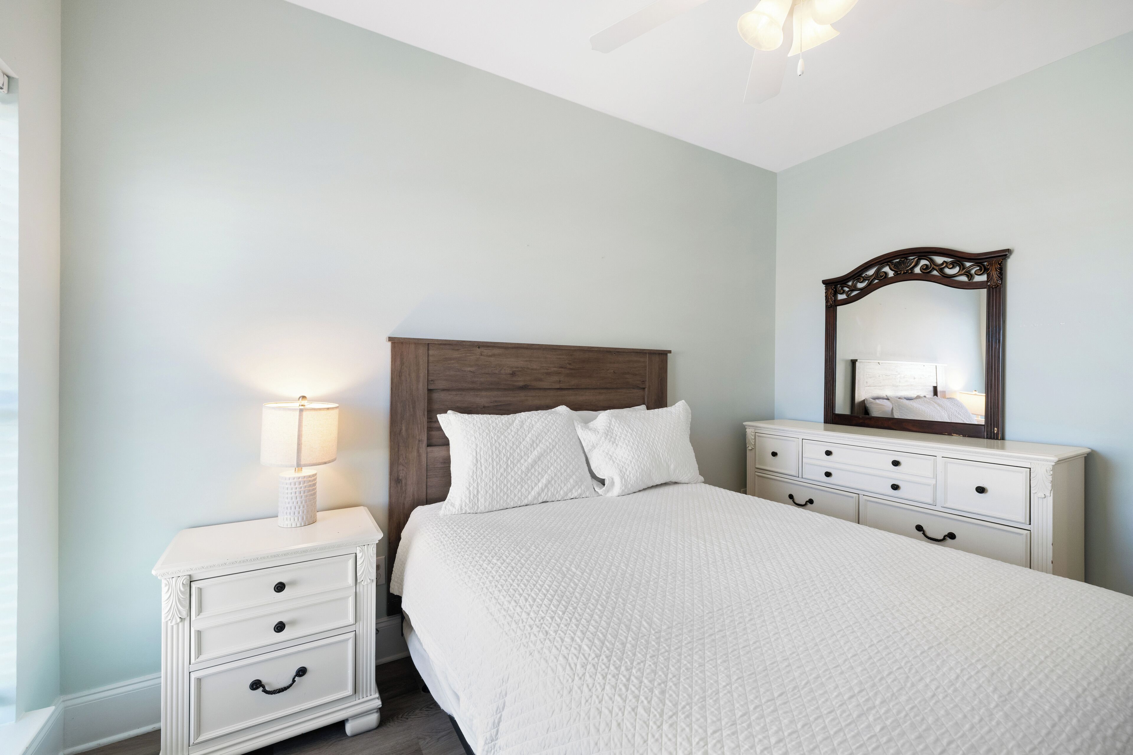 Een slaapkamer met een groot bed, een nachtkastje met een lamp, een dressoir en een spiegel aan de muur.