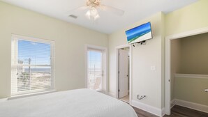 Een slaapkamer met een bed, een plafondventilator, een televisie aan de muur en uitzicht op het strand door het raam.