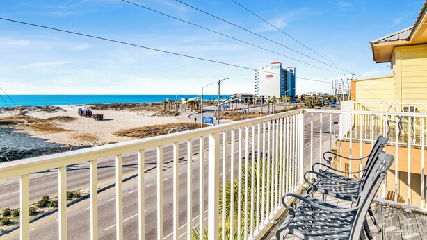 Een balkon met uitzicht op het strand en de oceaan, een weg met voertuigen, en een gebouw op de achtergrond.