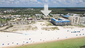 Une vue aérienne d’une station balnéaire comprenant plusieurs bâtiments, une plage de sable et une vue dégagée sur l’océan.