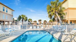 A swimming pool with lounge chairs and palm trees. - Kiran Terrace Quadplex by Liquid Life (Gulf Shores)