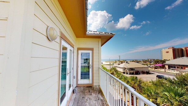 Un balcon avec vue sur la plage et l’océan, une porte blanche avec une fenêtre et une horloge au mur.